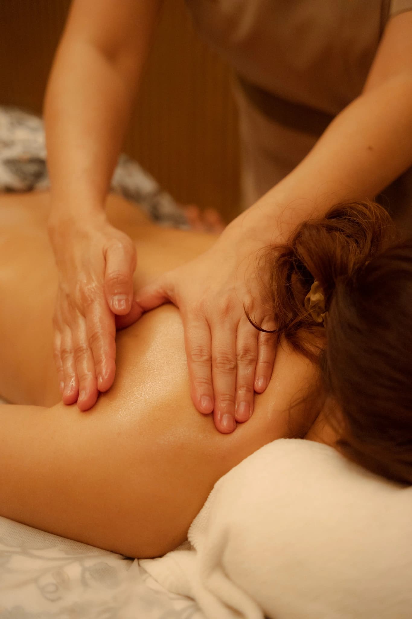 A therapist massaging a guest's shoulders in a warmly lit treatment room